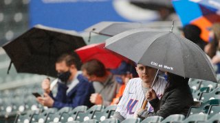 Fans wait out a rain delay under umbrellas during the first inning between the Miami Marlins and the New York Mets at Citi Field