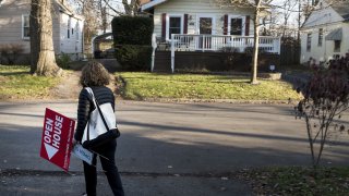 A real estate agent with an ‘Open House’ sign in the front yard of a home for sale.