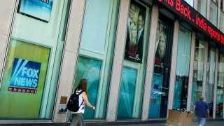 FILE- In this Aug. 1, 2017 file photo, people pass the News Corporation headquarters building and Fox News studios in New York. The parents of slain Democratic National Committee employee Seth Rich have reached a settlement of their lawsuit that alleged Fox News exploited their son's death in stories and commentary. Both sides confirmed the settlement on Tuesday, Nov. 24, 2020.