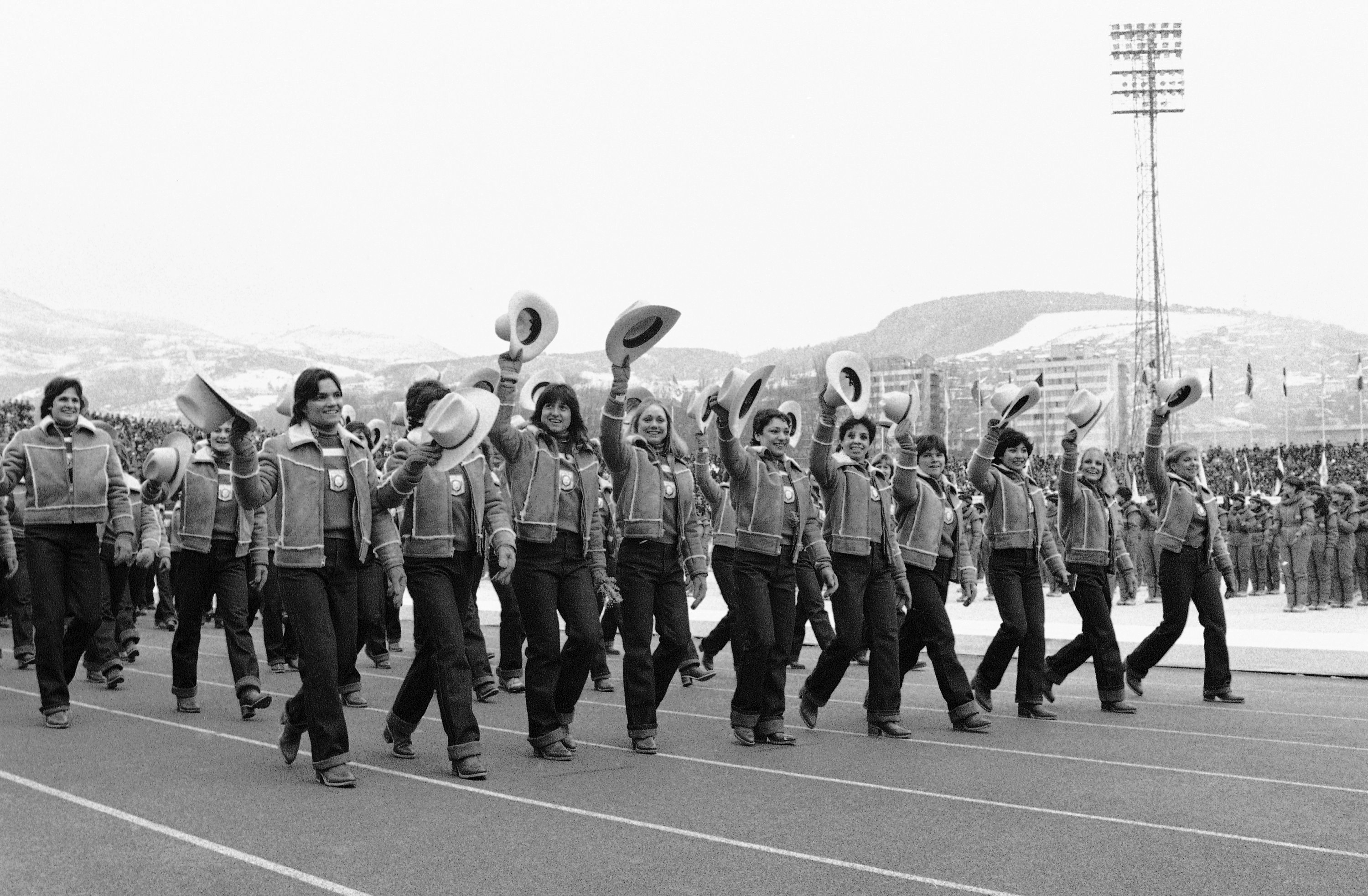 Atletas Olímpicos Americanos acenam com os chapéus de cowboy que fazem parte de seus uniformes Olímpicos oficiais em Fevereiro. 8 de 1984, quando Marcham no Estádio Kosevo durante as cerimônias de abertura dos jogos de Inverno em Sarajevo, Iugoslávia.