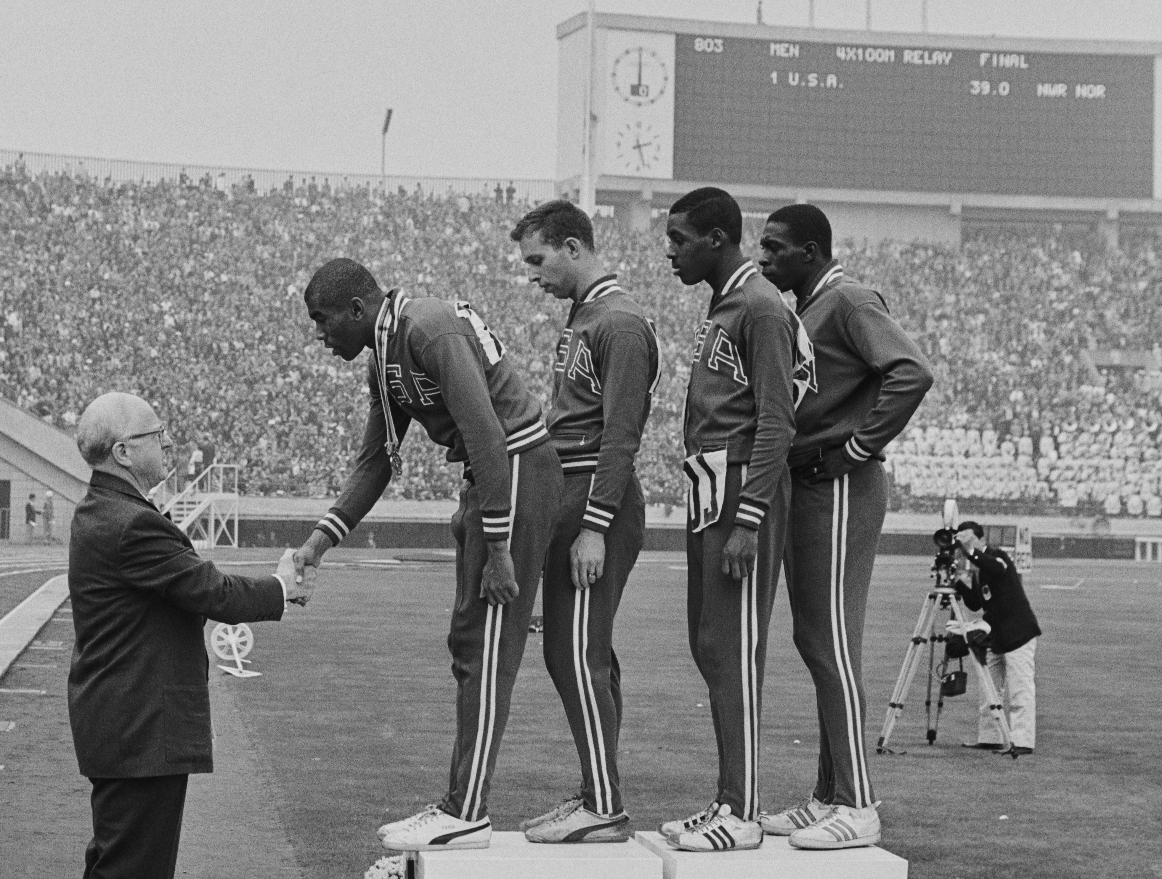 Avery Brundage, prezident Mezinárodního olympijského výboru, představuje vítězné zlaté medaile Otisovi Paulu Draytonovi, Geraldu Ashworthovi, Richardu Stebbinsovi a Robertu Hayesovi ze Spojených států během slavnostního ceremoniálu medailí Za vítězství v soutěži štafet mužů 4 x 100 metrů v říjnu. 21, 1964, během letních olympijských her v japonském Tokiu.