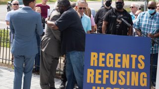 Jon Vaughn (R), former University of Michigan and former NFL football player, and Richard Goldman, a former UM student sports announcer, hug at a press conference on the University of Michigan campus on June 16, 2021 in Ann Arbor, Michigan.