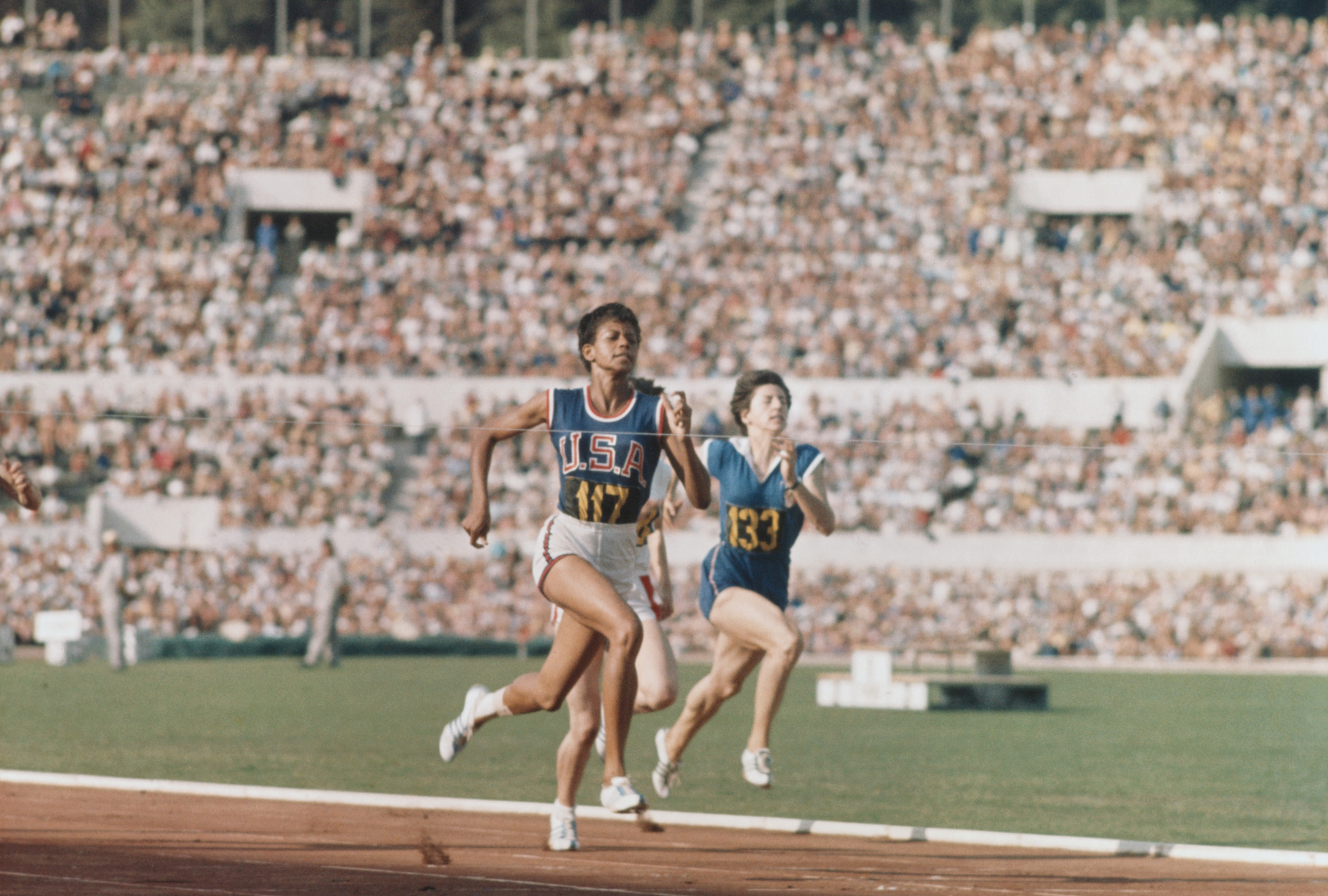 velocista Olímpico Americano Wilma Rudolph nas etapas finais de uma corrida nos jogos de Verão de 1960. Rudolph, que não podia andar sem o uso de chaves até os nove anos, ganhou o ouro na Corrida de 100 e 200 metros e ancorou a equipe vencedora de revezamento de 400 metros.