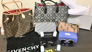 Counterfeit goods laid out on a table, including a fake Louis Vuitton bag, Givenchy shirt, Cialis pills, Chanel sunglasses and more. The goods were seized by U.S. Customs and Border Protection.