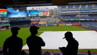 Fans wait for the rain to stop before a baseball game between the New York Yankees and the New York Mets at Yankee Stadium