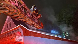 Firemen stand on a crane over a house.