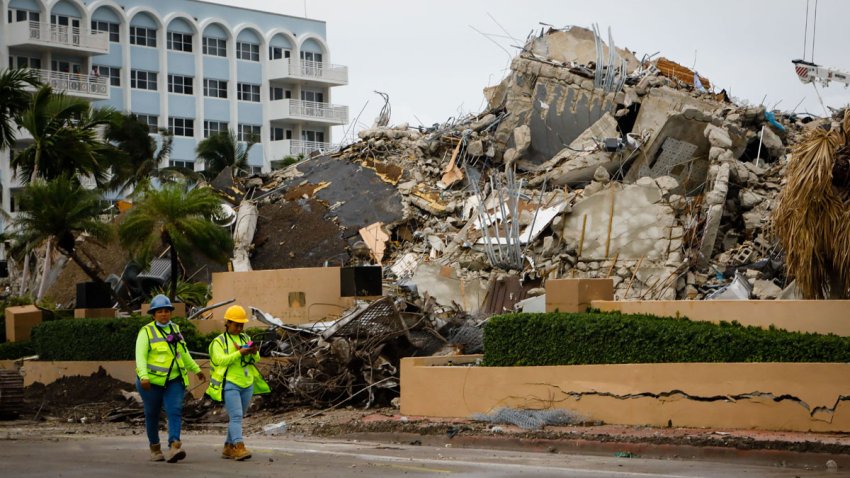 Workers walk past the rubble of the collapsed building Champlain tower in Surfside, Florida on July 6, 2021. – Rescuers raced to search the site of a deadly condo tower collapse in Florida as Tropical Storm Elsa barreled closer, threatening the operation with torrential downpours and strong winds. The death toll from the June 24 disaster in Surfside rose overnight to 32 as search teams found four more bodies in the rubble, Miami-Dade County Mayor Daniella Levine Cava told reporters. (Photo by Eva Marie UZCATEGUI / AFP) (Photo by EVA MARIE UZCATEGUI/AFP via Getty Images)