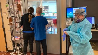 two visitors peer into the room of a COVID-19 patient in the intensive care unit at Salem Hospital in Salem, Ore.