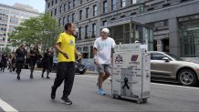 Paul Veneto, right, is joined by Boston Marathon Race Director Dave McGillivray, front left, as Veneto pushes a beverage cart along State Street, in Boston