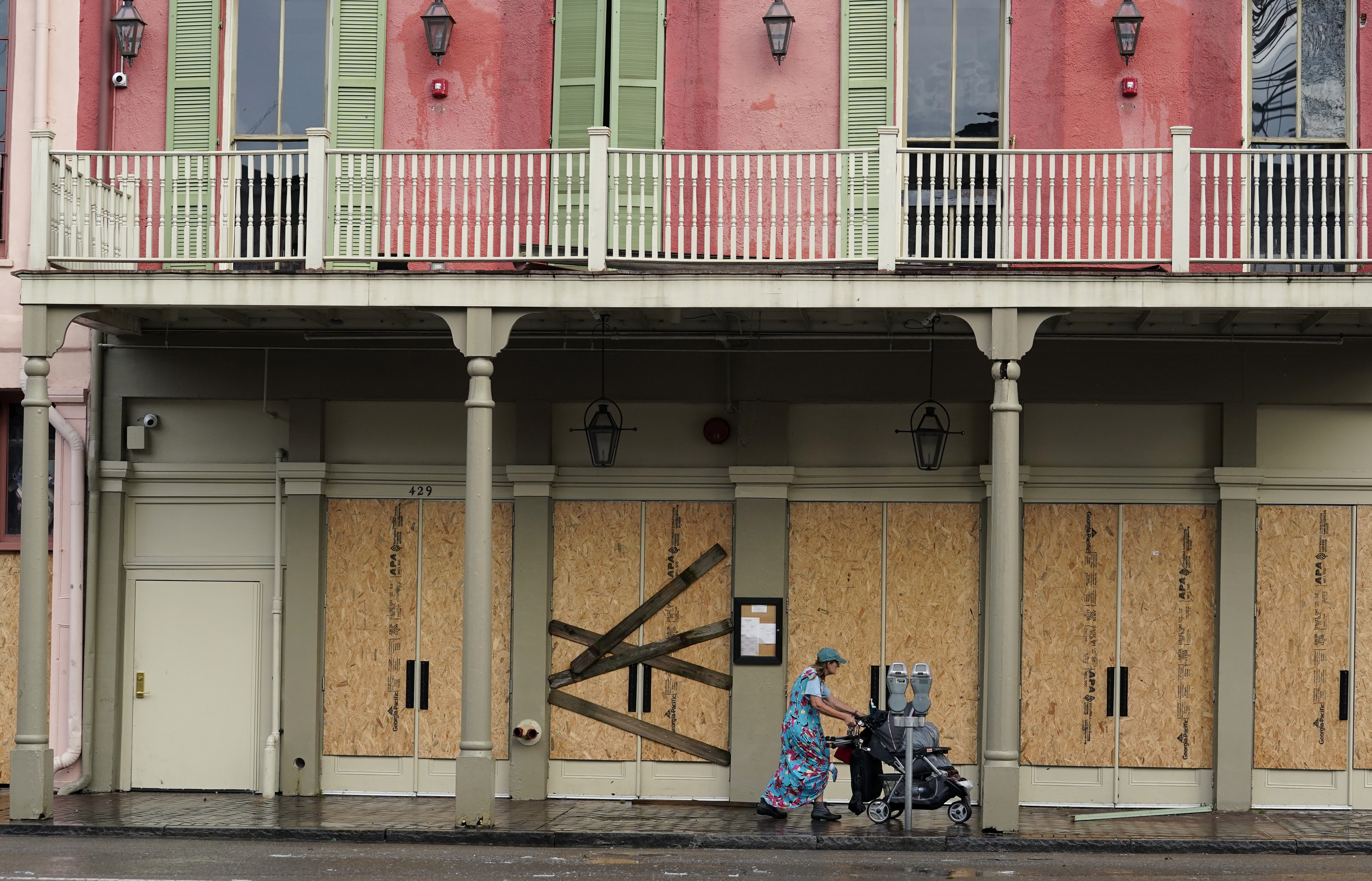 A woman pushes a stroller past a boarded-up building in the French Quarter after the effects of Hurricane Ida knocked out power to the city, Monday, Aug. 30, 2021, in New Orleans, La.