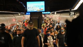 Commuters wearing masks disembark from a Metro-North train during the morning rush hour commute