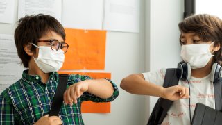 Boys wearing masks giving elbow bump while standing against wall in school