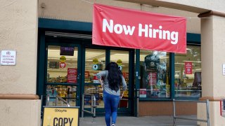 A Now Hiring sign hangs near the entrance to a Winn-Dixie Supermarket