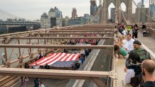 People watch as demonstrators march across the Brooklyn Bridge to protest the Covid-19 vaccine mandate for municipal workers on October 25, 2021 in New York City. All city workers, excluding uniformed correction officers, are required to have at least one dose of the COVID-19 vaccine by 5pm on October 29th. 