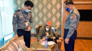 In this photo provided by the Myanmar Military True News Information Team, released American journalist Danny Fester writes on a document while seated between two police officers at the Naypyitaw International Airport in Naypyitaw, Myanmar Monday, Nov. 15, 2021. Fenster, who was recently sentenced to 11 years of hard labor after spending nearly six months in jail in military-ruled Myanmar, has been freed. A former U.S. diplomat who helped negotiate the release said Fenster was on his way home Monday.