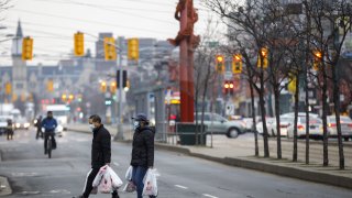 Pedestrians wearing protective masks carry grocery bags