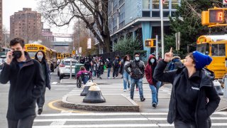 Pedestrians cross Houston Street as students wearing masks leave the New Explorations into Science, Technology and Math (NEST+m) school in the Lower East Side neighborhood of Manhattan on Tuesday, Dec. 21