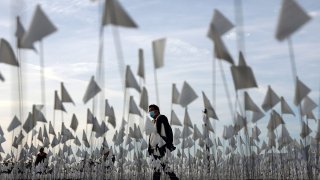 FILE - A person wearing a face covering walks past a white flag memorial installation outside Griffith Observatory honoring the Los Angeles County residents who have died from COVID-19 on Nov. 18, 2021, in Los Angeles, California.
