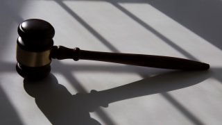 gold-trimmed wooden judicial gavel over shadow of bars.