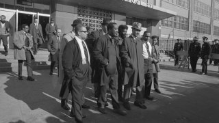 Led by the Rev. C. Herbert Oliver (wearing rain hat), members of the Ocean Hill-Brownsville local school governing board leave Brooklyn Junior High School 271. In an effort to improve test scores and help students, New York State attempted an experiment to decentralize three school districts; they appointed school governing boards that would give the mostly minority parents more say in school matters. When the board fired 13 teachers and 6 administrators, saying they were impeding the decentralization process, the United Teacher's Federation union organized several strikes throughout the fall to close down the schools.