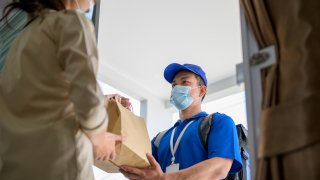 Male courier with bicycle delivers bag with food to the client's door.