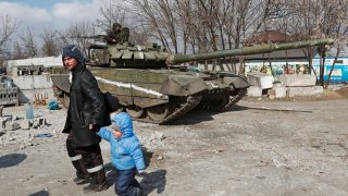 A local resident walks with a child past a tank of pro-Russian troops during Ukraine-Russia conflict in the besieged southern port city of Mariupol, Ukraine March 18, 2022.