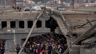 Ukrainians crowd under a destroyed bridge as they try to flee across the Irpin River in the outskirts of Kyiv, Ukraine, Saturday, March 5, 2022.