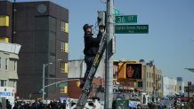 A member of the NYPD retrieves a security camera near a subway station in New York City on April 12, 2022, after at least 16 people were injured during a rush-hour shooting in the Brooklyn neighborhood of Sunset Park.