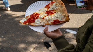 A tourist carries a freshly made slice of pizza in New York City. (Photo by Robert Nickelsberg/Getty Images)