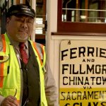 Cable Car gripman Valentine Lupiz stands in front of historic car Big 19 in SFMTA's cable car barn.