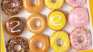 Pink Strawberry-frosted donuts, chocolate-frosted donuts, glazed, and yellow donuts lined up with "2022" written in frosting across them.