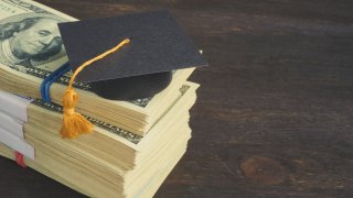 Savings for education and university concept. Stack of cash and graduation cap.