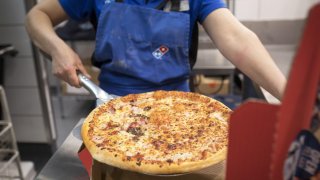 An employee places a cooked pizza into a delivery box inside a Domino’s Pizza Group Plc store.