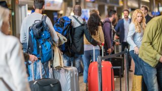 FILE - Travelers standing with luggage in queue at airport arrival area.