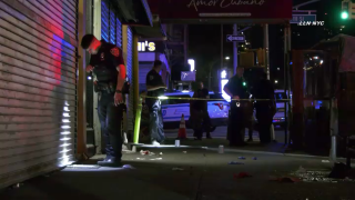 Police officer uses flashlight to examine shooting scene in Harlem.