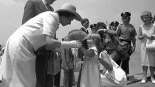 UNITED STATES - JULY 10: A Royal Welcome, Queen Elizabeth stoops to take a welcoming bouquet from Mayor Beame's granddaughter. Julie. at Battery Park . Watching is Gov. Carey. Sailing into the harbor on board the royal yacht, Britannia, she was greeted by a 21-gun salute. Later, she received cheers of welcome from large crowds on tour of city. At Federal Hall, the queen was made an honorary citizen of city. (Photo by Harry Hamburg/NY Daily News Archive via Getty Images)