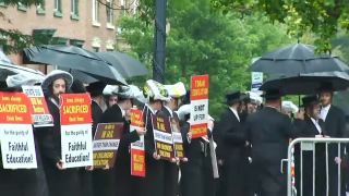 Ultra-Orthodox and Hasidic Jewish community members hold signs at a rally to protest new requirements for private schools following a bombshell New York Times investigation.