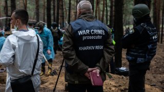 War crime prosecutor of Kharkiv Oblast stands with forensic technician and policeman at the site of a mass burial in a forest during exhumation on September 16, 2022 in Izium, Ukraine.