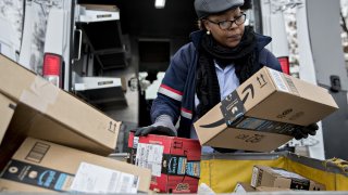 A letter carrier holds Amazon.com packages while preparing a vehicle for deliveries at a United States Postal Service processing and distribution center in Washington, D.C.