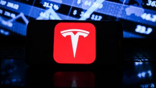 In this photo illustration a Tesla logo seen displayed on a smartphone with the stock market graphic in the background.