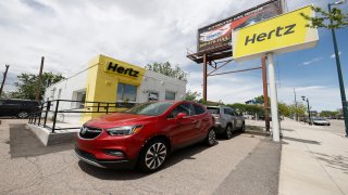 This May 23, 2020, photo shows rental vehicles parked outside a closed Hertz car rental office in south Denver.
