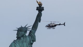 A doors off FlyNYON tourist helicopter flies past the Statue of Liberty at sunset in New York City on July 1, 2020 as seen from Jersey City, New Jersey. (Photo by Gary Hershorn/Getty Images)