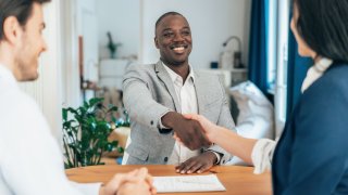 Business people in the office sitting on desk and shaking hands, document in front of them