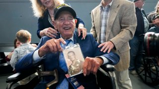 World War II veteran Joseph Eskenazi, who at 104 years and 11 months old is the oldest living veteran to survive the attack on Pearl Harbor, holds a photo of his younger self, at an event celebrating his upcoming 105th birthday at the National World War II Museum in New Orleans, Wednesday, Jan. 11, 2023.