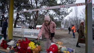 A woman lays flowers at a bus stop, for people who were killed in a Russian missile strike on an apartment building in the southeastern city of Dnipro, Ukraine, Monday, Jan. 16, 2023.