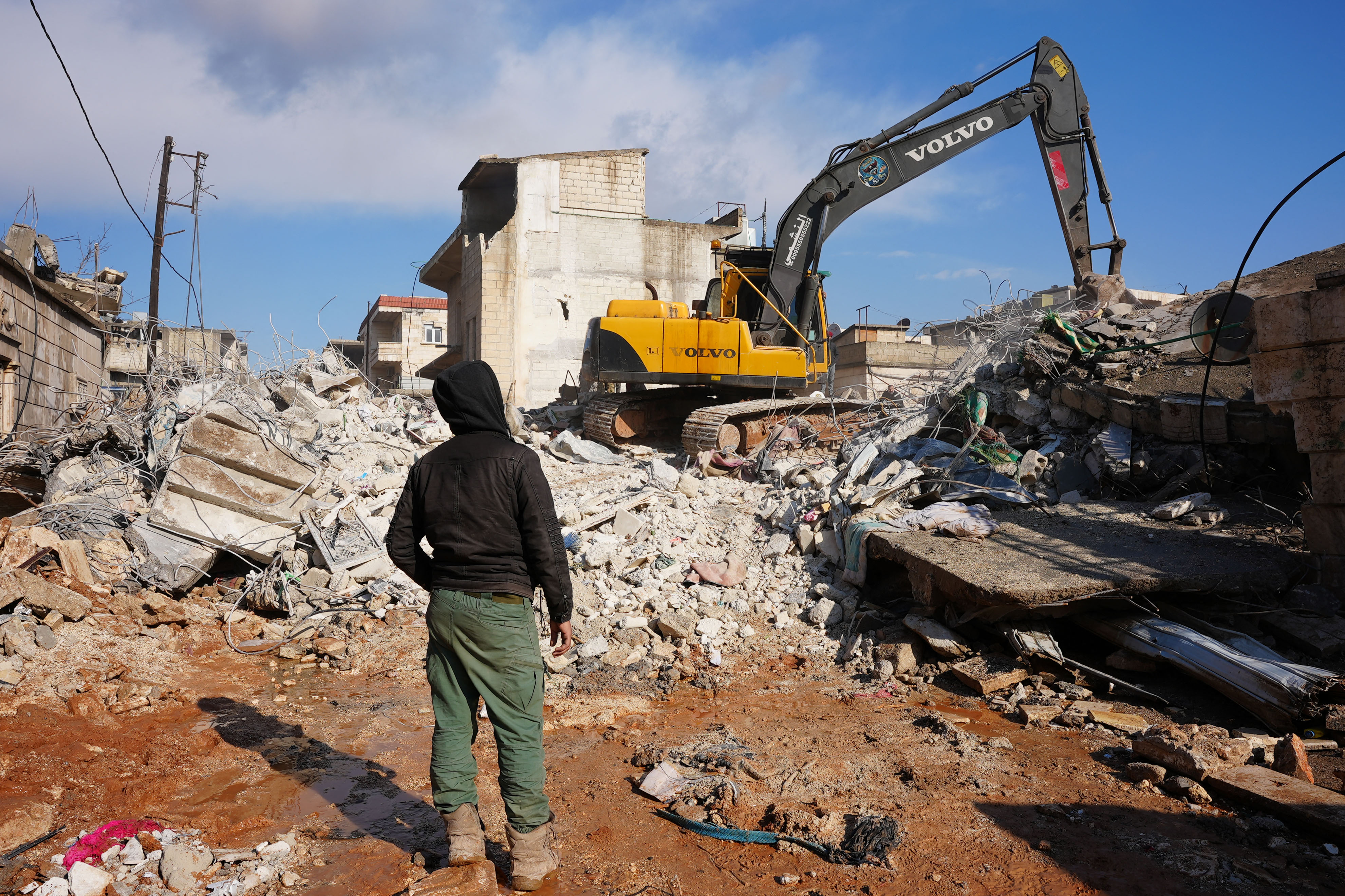 A Syrian boy watches an excavator go through the rubble of a house in which an entire family, save a newborn baby, was killed, Feb. 7, 2023, in the town of Jandaris, Syria, following a deadly earthquake. Residents and rescue workers uncovered a newborn survivor trapped under rubble, her umbilical chord still tied to her mother, who died when the building collapsed.