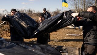 Men carry bags containing three freshly exhumed bodies in a cemetery on the outskirts of Borodyanka, Ukraine, Thursday, March 2, 2023.