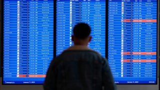 FILE – A traveler looks at a flight board with delays and cancellations at Ronald Reagan Washington National Airport in Arlington, Va., Wednesday, Jan. 11, 2023.