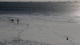 FILE - A fisherman checks his line in the mud flats as commercial fishing boats anchor in Bristol Bay, Alaska, during low tide.