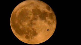 A commercial airliner flies Northwest across Lake Michigan in front of the "Full Buck" supermoon